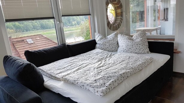 A bedroom with a large bed, a sofa, and a view of a green landscape through the windows. - Bungalow "Schönblick" am Elberadweg in Pirna by Interhome (Pirna)