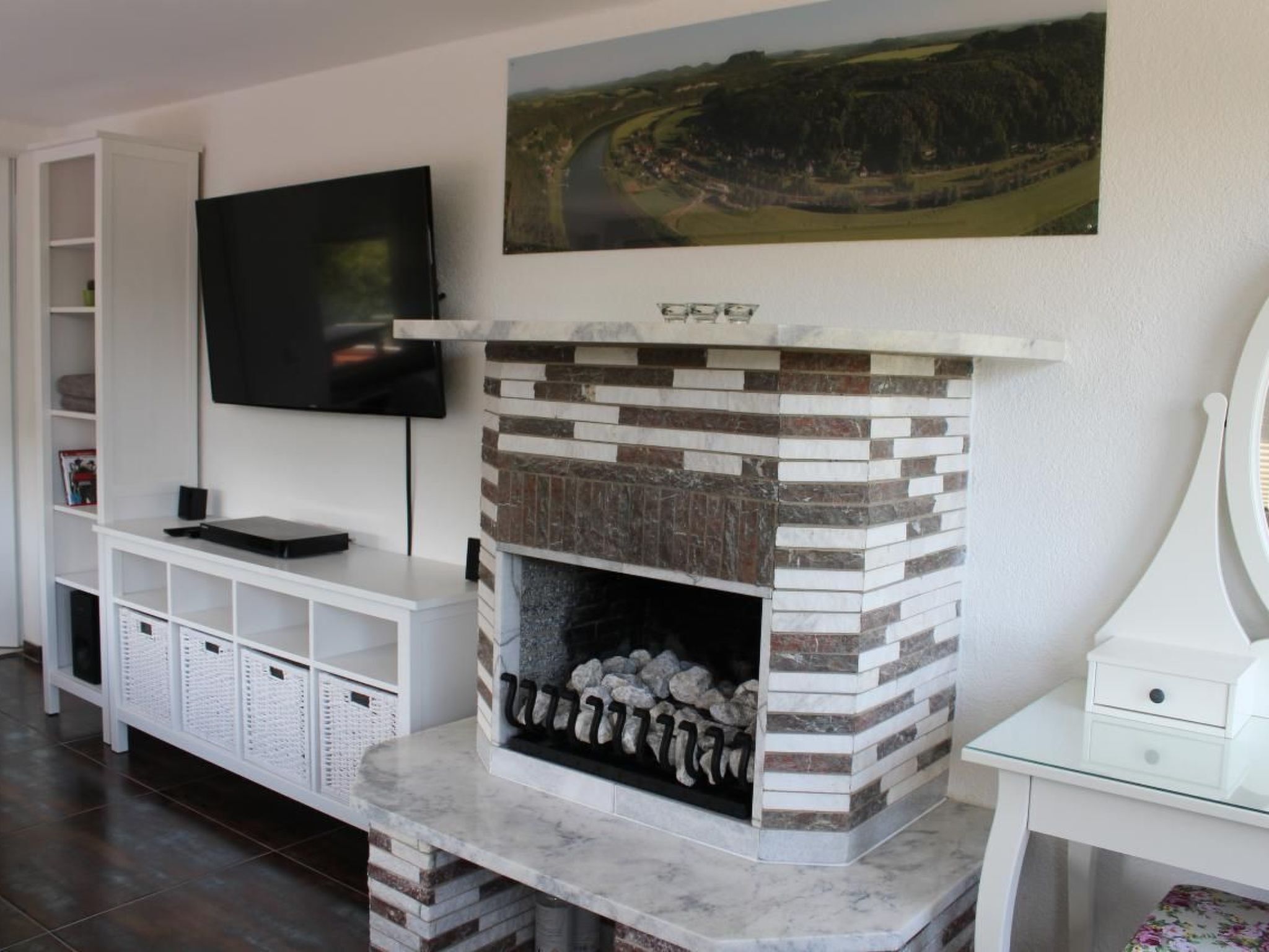 Una sala de estar con chimenea de piedra, un televisor de pantalla plana montado en la pared y una estantería.