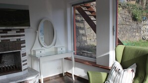A room with a stone fireplace, a white vanity with a mirror, and a green armchair with a striped pillow. - Bungalow "Schönblick" am Elberadweg in Pirna by Interhome (Pirna)