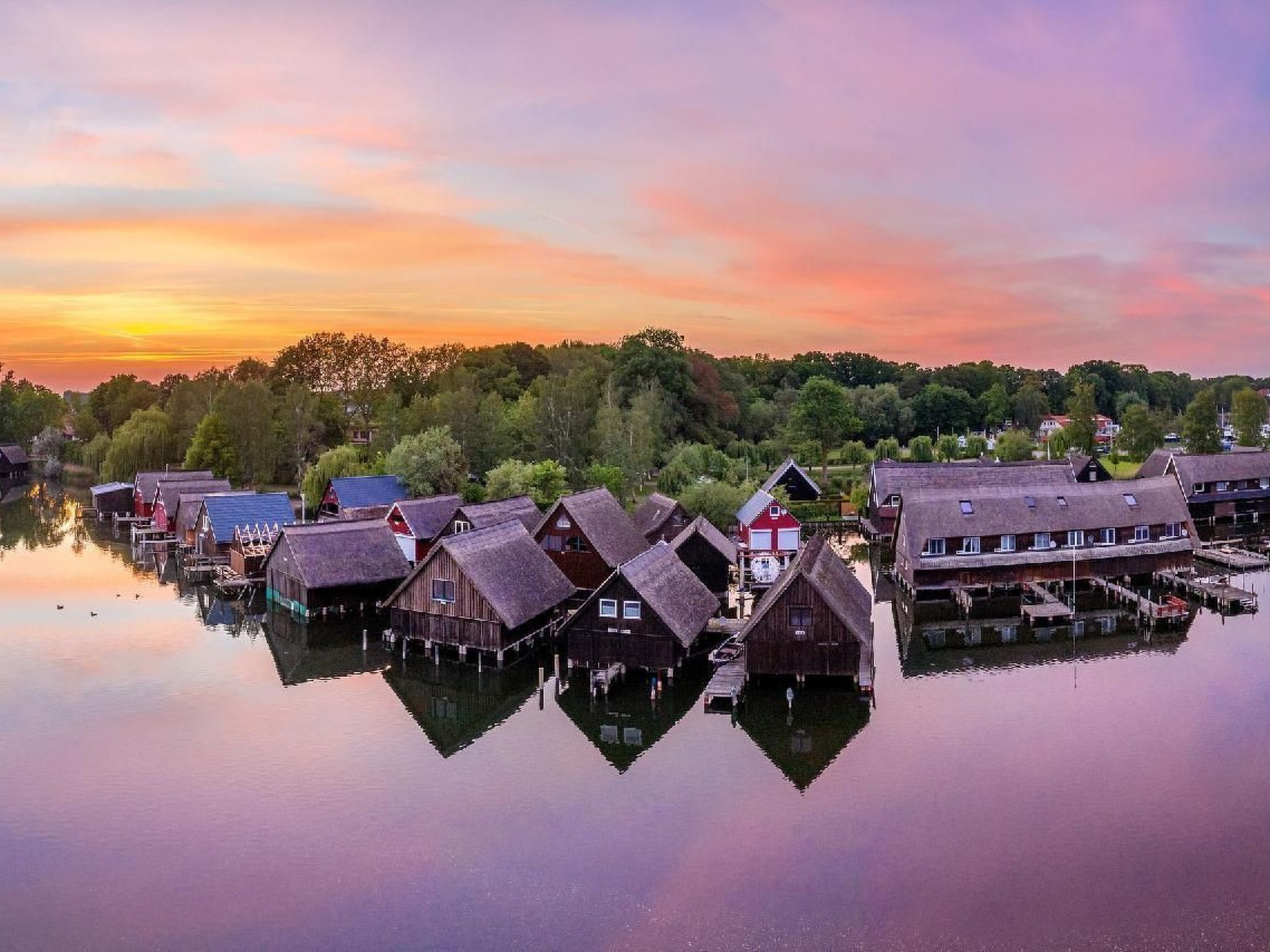 A waterfront village with traditional wooden houses, calm water, and a sunset sky.