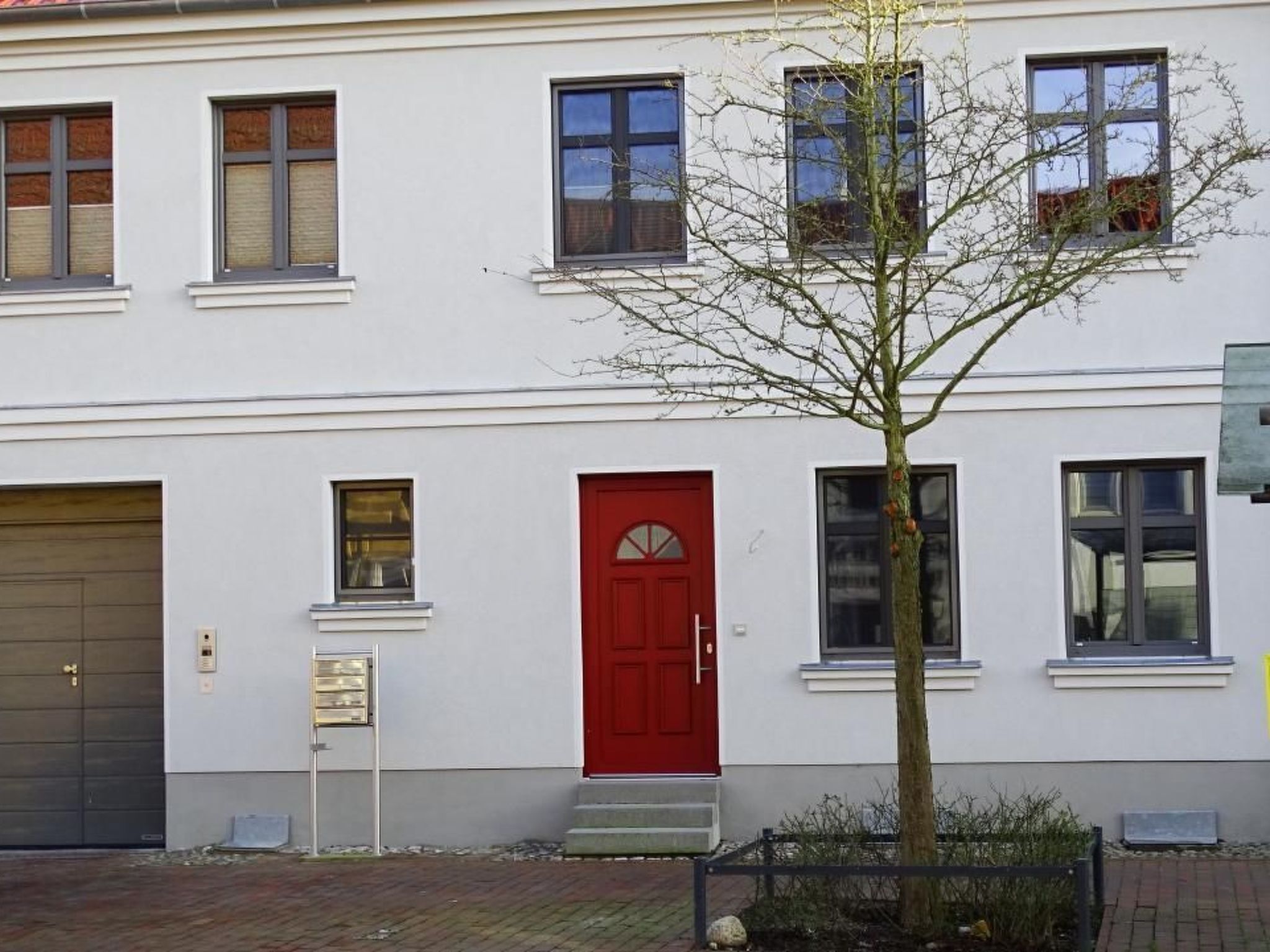Ein zweistöckiges Gebäude mit roter Tür, Fenstern und einem Baum davor.