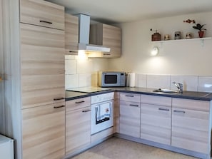 Eine moderne Küche mit hellen Holzschränken, einer eingebauten Mikrowelle und einem Edelstahl-Spülbecken.
