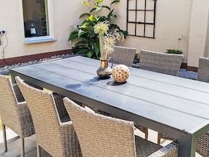Une table de jardin rectangulaire, conçue pour être utilisée à l’extérieur, avec un cadre en métal et entourée de chaises en osier.