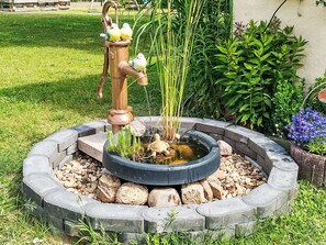 Un jardin avec une bordure circulaire en pierre, un petit étang et un abreuvoir à oiseaux où se trouvent deux oiseaux.