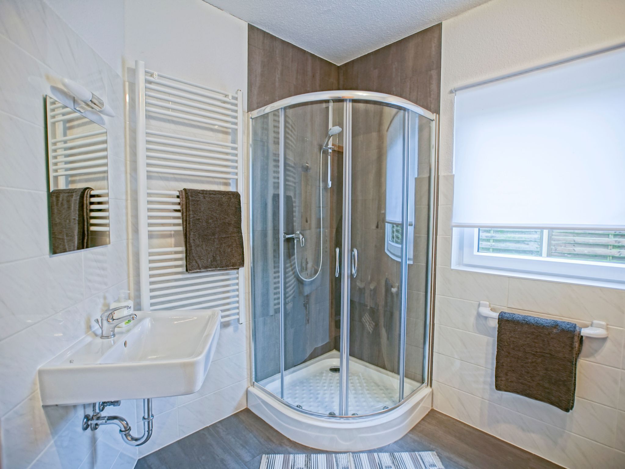 A modern bathroom with a glass-enclosed shower, a white sink, and a towel rack.