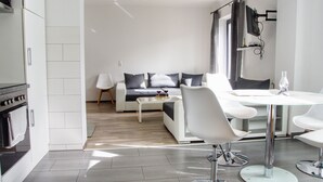 Eine moderne Küche mit weißen Schränken, einem Einbauofen und einem Essbereich mit einem Glastisch und weißen Stühlen.