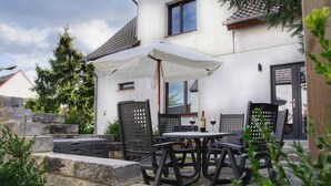Eine Terrasse mit Tisch und Stühlen, einem weißen Sonnenschirm und einer Steinmauer.
