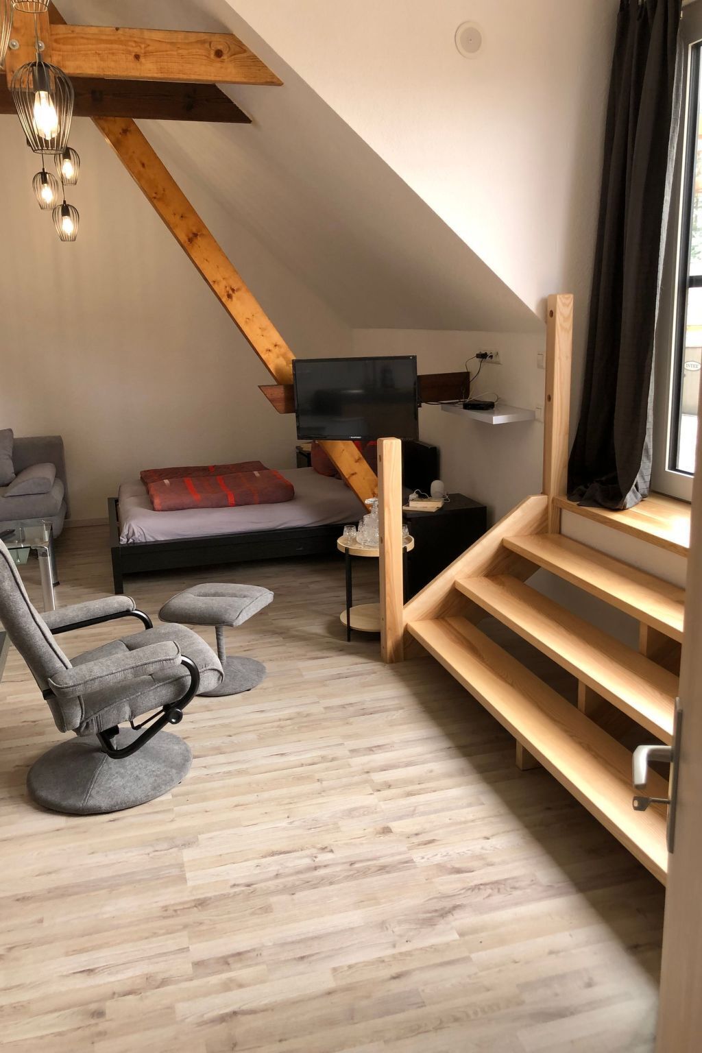 Une pièce de style loft avec un plafond en pente, un lit, une télévision, une chaise et une petite table.