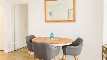 A room with a round wooden table, four grey chairs, a blue vase, and a framed picture on the wall.