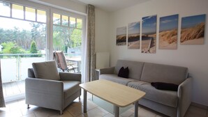 A living room with a sofa, armchair, and a small table. There are three beach-themed pictures on the wall. - Appartement in Koserow mit Grill und Garten by Interhome (Koserow)