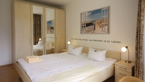 A bedroom with a large bed, a wardrobe, a bedside table with a lamp, and a wall with a framed picture. - Appartement in Koserow mit Grill und Garten by Interhome (Koserow)