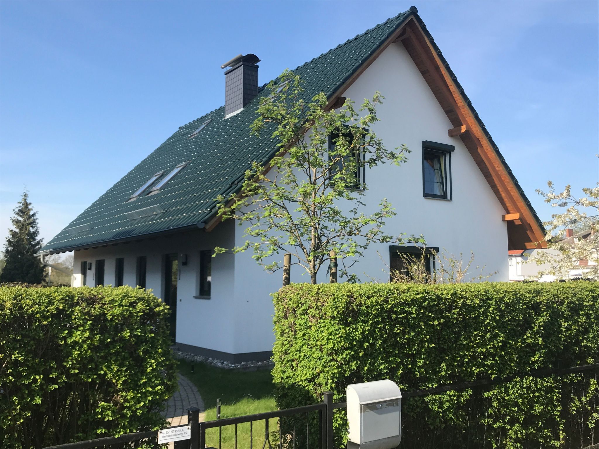 A two-story house with a green roof, white walls, and a small attached garage.