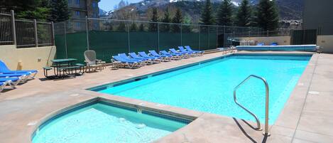 A rectangular swimming pool with a diving board, surrounded by blue lounge chairs and a green fence.