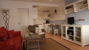 Un espacio habitable pequeño con sofá rojo, mesa de mimbre, zona de cocina y televisor sobre un mueble.