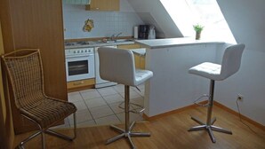 Keittiössä on sisäänrakennettu uuni, kahvinkeitin ja ikkuna. Siellä on myös kaksi valkoista baarijakkaraa ja yksi rottinkituoli.