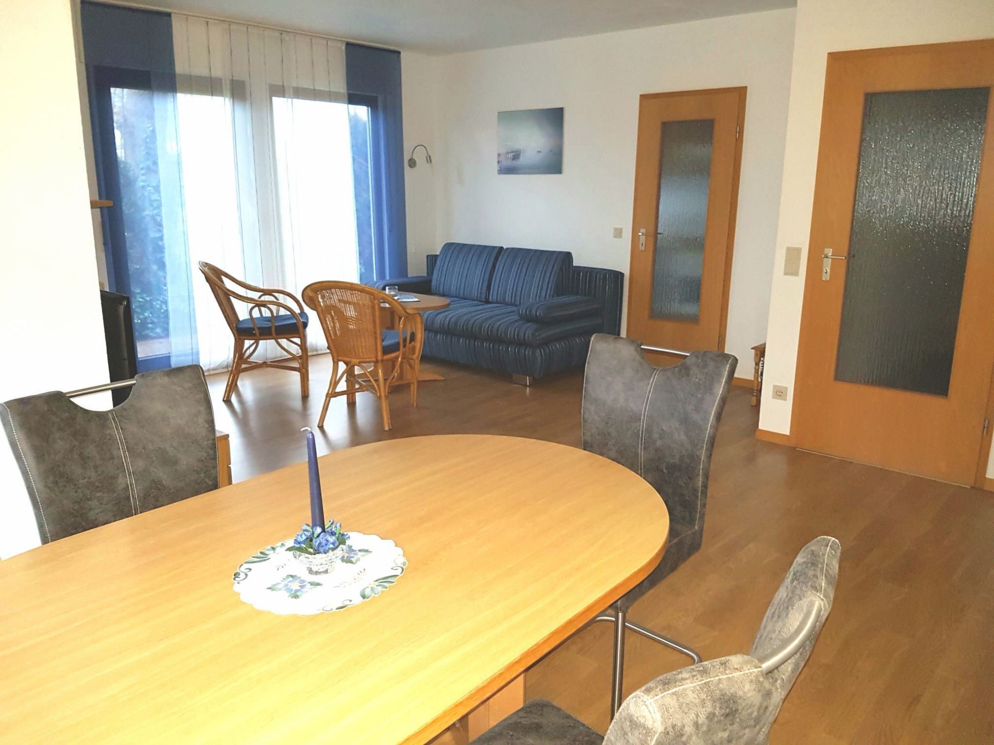 Een eethoek met een houten tafel en stoelen, een blauwe bank en een deur met geëtste glaspanelen.