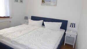 Ein ordentlich bezogenes Bett mit weißer Bettwäsche und einem blauen Kopfteil in einem Zimmer mit weißen Wänden.