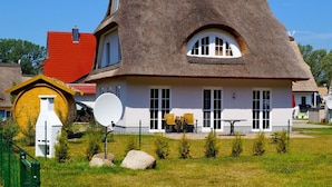 Una casa con tetto di paglia, pareti bianche e un piccolo giardino con tavolo e sedie.