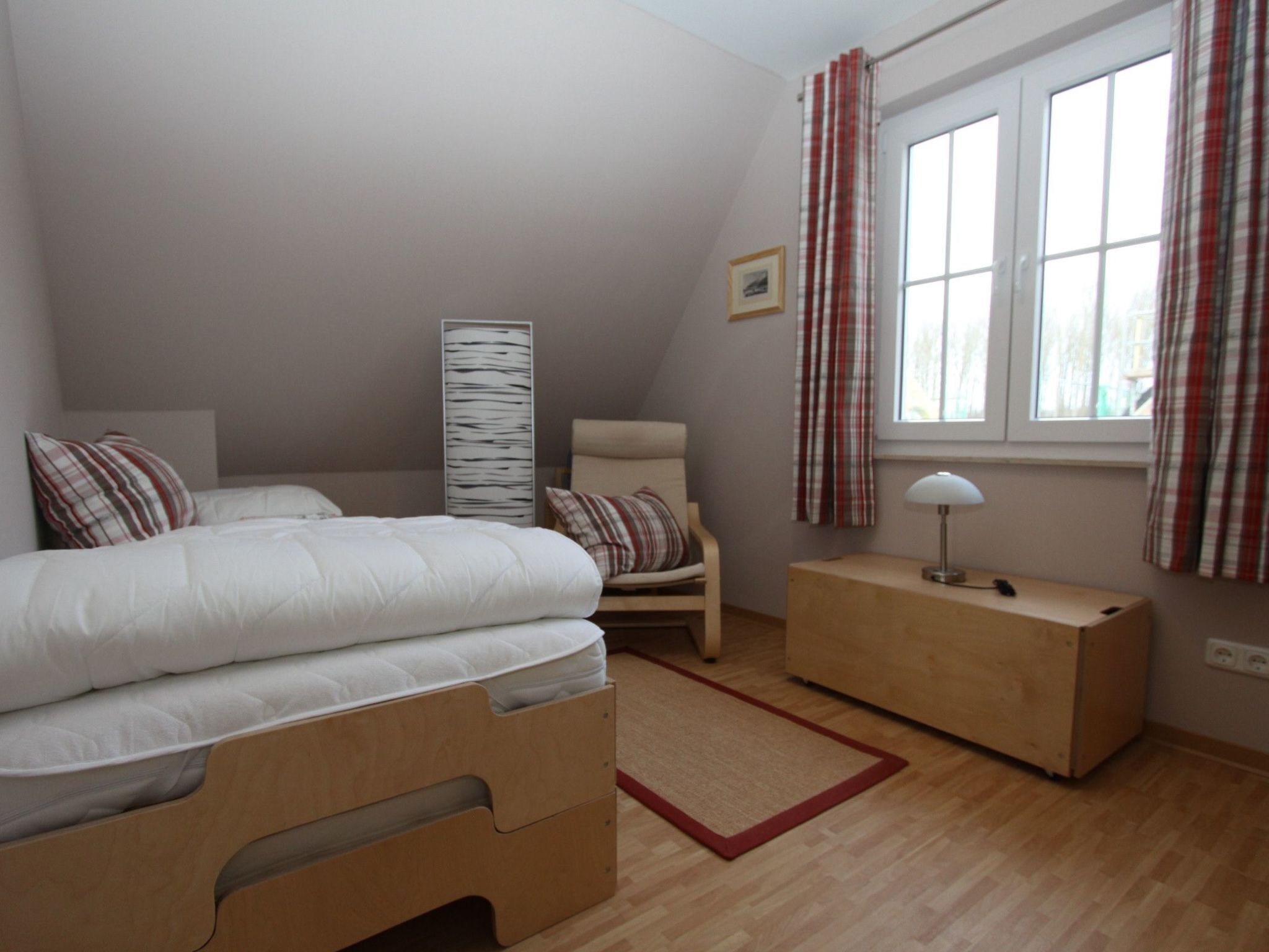 A bedroom with a bed, a chair, a bedside table, a lamp, and a window with curtains.