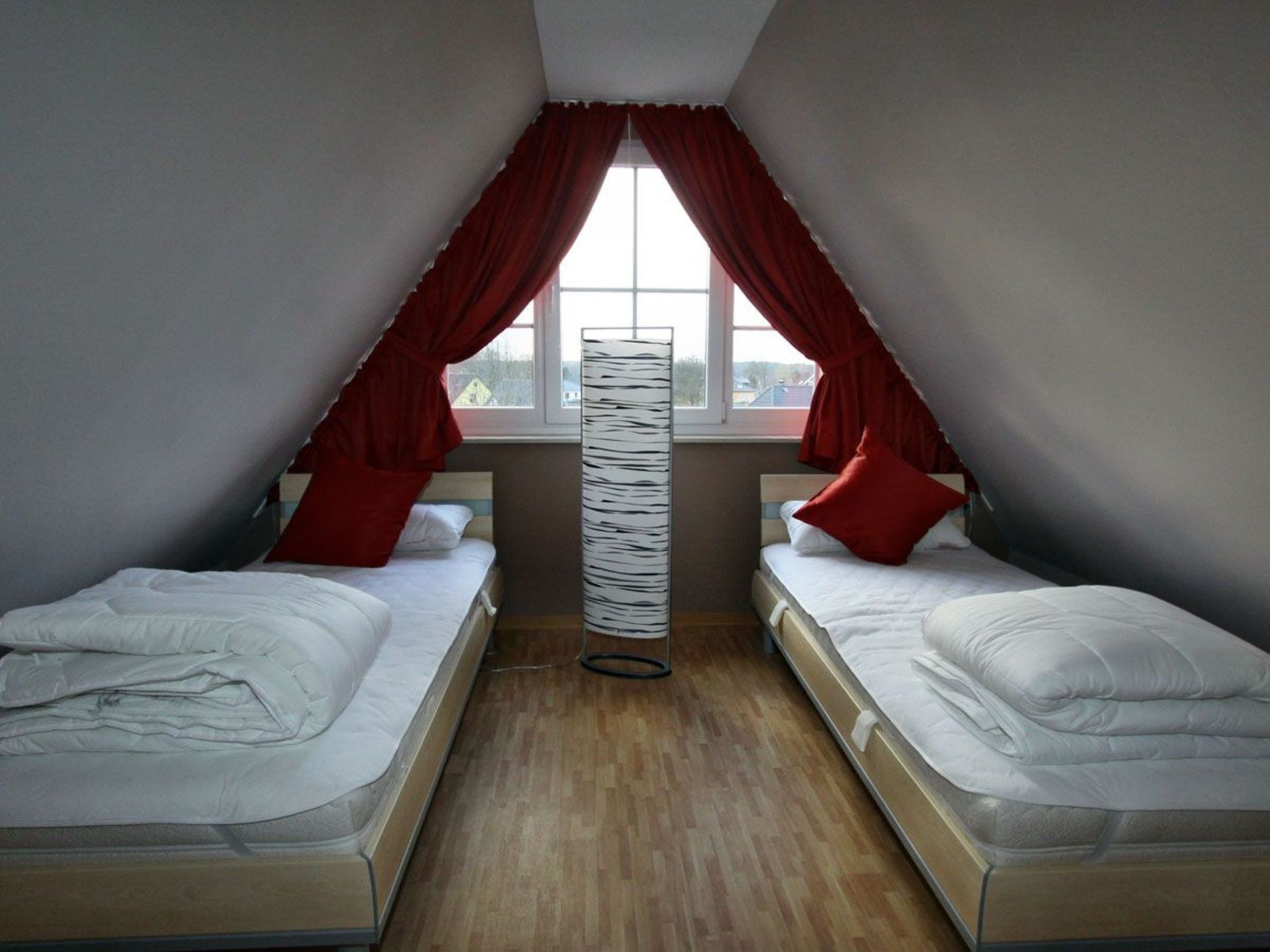 Une chambre de dortoir avec deux lits, une fenêtre avec des rideaux rouges et un lampadaire.