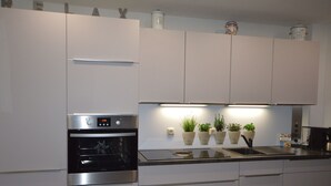 Una cuina moderna amb armaris blancs, un forn d'acer inoxidable i un rentaplat amb encimera.