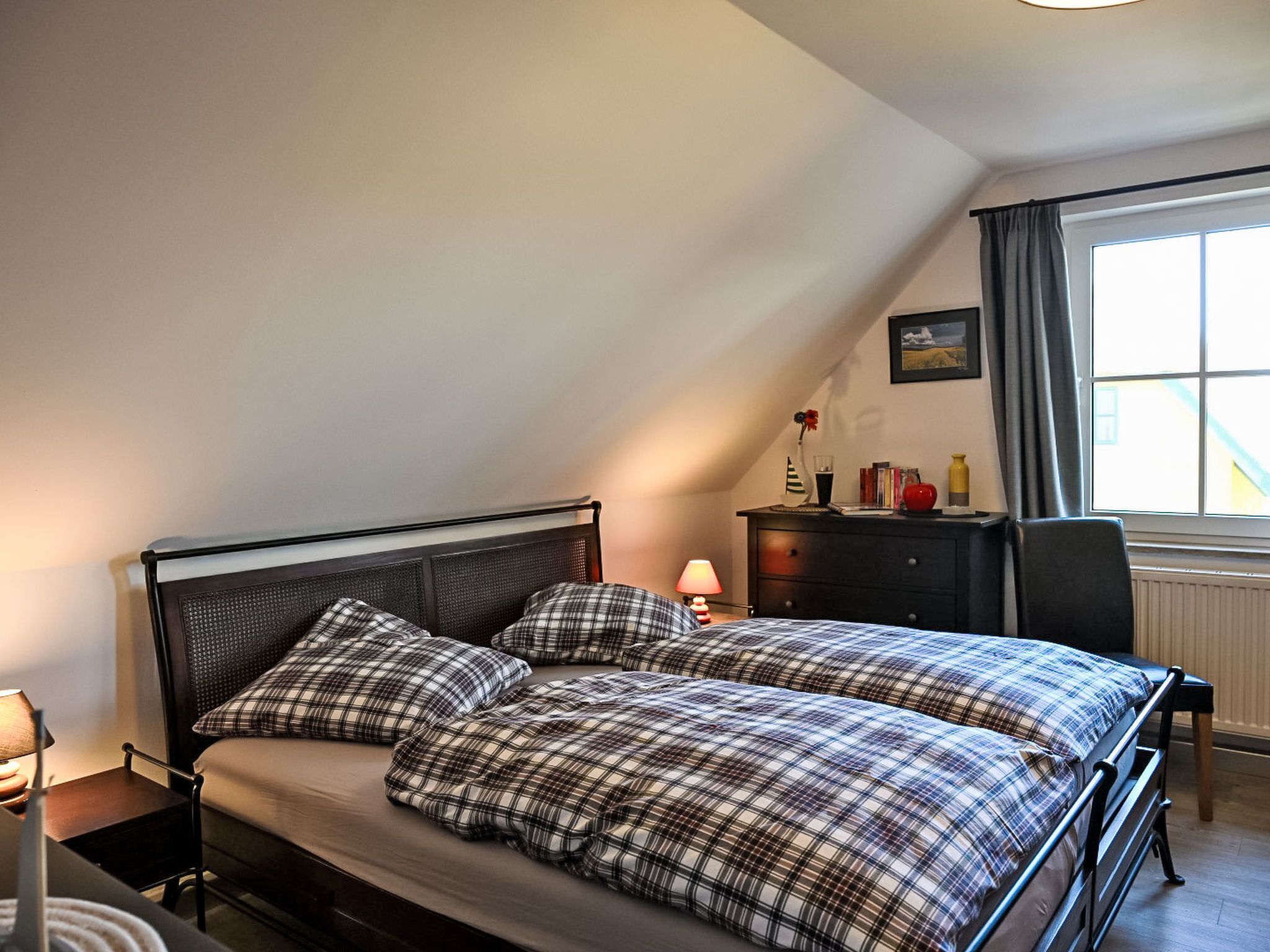 A bedroom with a bed, a dresser, a lamp, and a window.