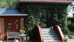 En liten byggnad med ett rött tegeltak, en entré av tegel och en bänk med solrosor utanför.