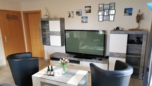 A modern living room with a flat-screen TV, two black leather sofas, a coffee table with drinks and a vase, and a grey cabinet with shelves. - Apartment Breege by Interhome (Breege)