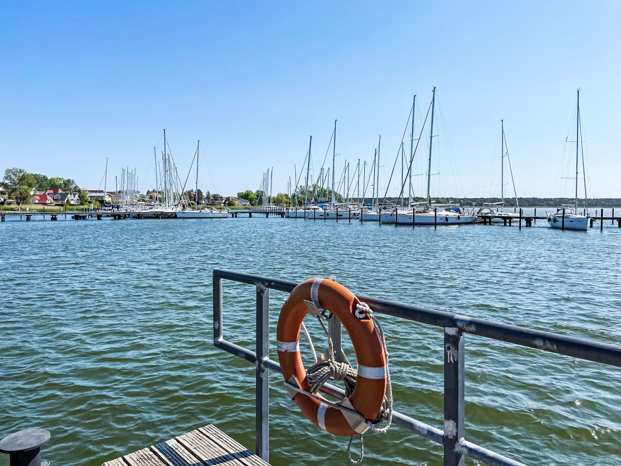 A marina with boats docked, a lifebuoy attached to a railing, and a clear sky.