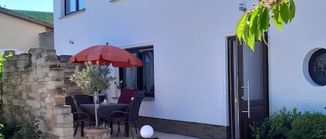 Eine Terrasse mit Tisch, Stühlen, einem roten Sonnenschirm und Blumentöpfen.