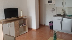 A compact living space with a TV on a wooden stand, a small shelf with books, a microwave, and a kitchenette with cabinets and a stove. - in Tarnewitz mit Terrasse und Grill by Interhome (Boltenhagen)
