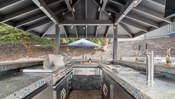 Une cuisine extérieure équipée d’un barbecue, d’un évier et d’un coin bar, le tout installé sous une structure abritée.