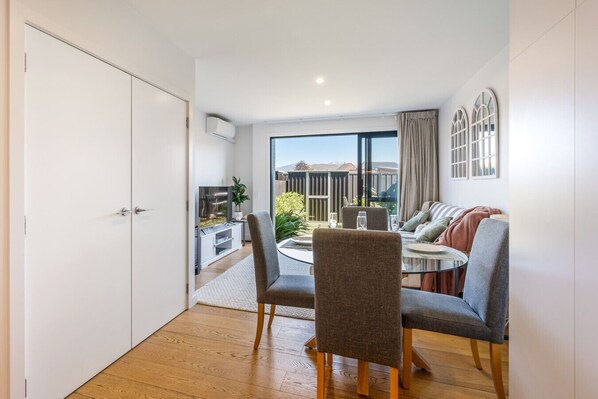 A modern living room with a dining area, large windows, and a view of the outdoors.