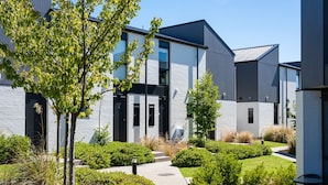Un edificio moderno con un design pulito e minimalista, caratterizzato da un mix di materiali in cemento e metallo, immerso nel verde e circondato da vialetti curati.