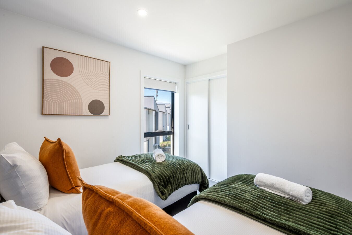 Une chambre d’hôtel moderne avec deux lits, une grande fenêtre et une œuvre d’art murale au style minimaliste.