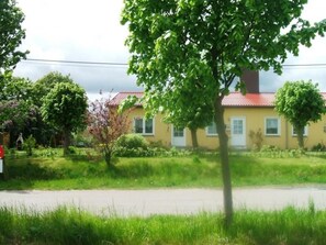 Ein gelbes Haus mit rotem Dach, umgeben von Grünflächen und einer Straße.