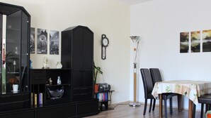 Un salon comprenant un meuble de rangement noir pour appareils multimédias, une table à manger avec des chaises, un lampadaire et des œuvres d’art murales.