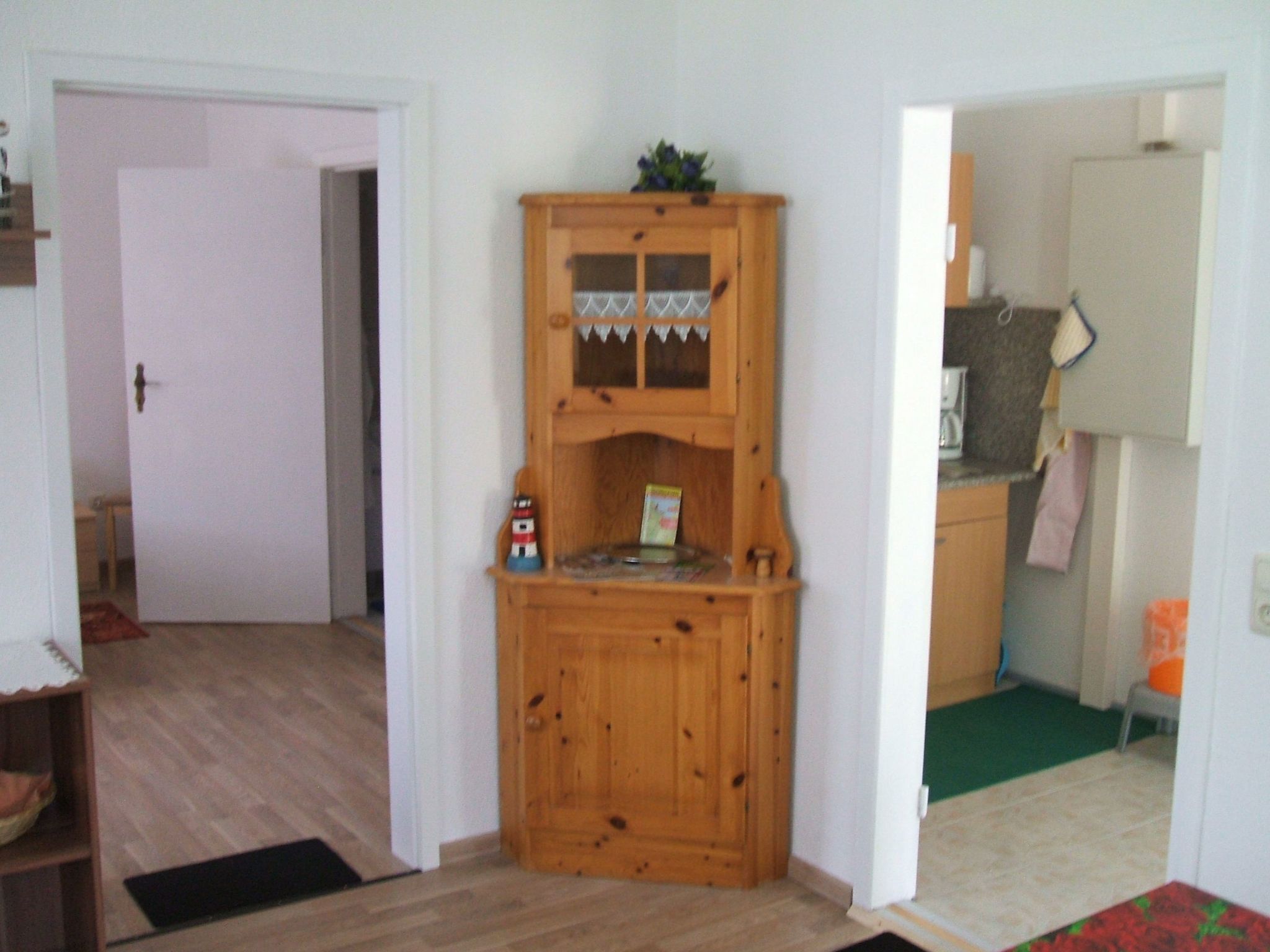 Habitación de esquina con un armario de madera, una puerta y un estante pequeño con objetos.