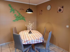Un comedor con una mesa cubierta por un mantel escocés, dos sillas, un jarrón con flores, una lámpara colgante y un mapa mural.
