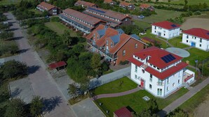 Vista aérea de una zona residencial con varias casas, un edificio grande con techo rojo y una masa de agua al fondo.