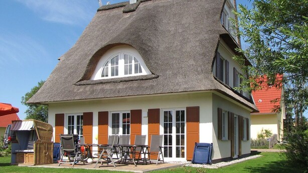 Een huis met een steil dak, een groot rondboogvenster en een voortuin met buitenmeubilair.