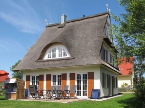 Ein Haus mit einem steilen Satteldach, einem großen Bogenfenster und einer Veranda mit Gartenmöbeln.