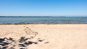 Een zandstrand met een helderblauwe lucht en een rustige zee.