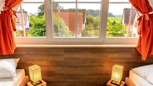 Een slaapkamer met twee bedden, houten nachtkastjes en uitzicht op een tuin door een raam.