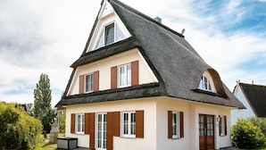 Een huis met twee verdiepingen, een steil dak, witte muren en bruine luiken.