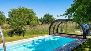 A swimming pool with a glass enclosure, surrounded by lush greenery and trees. - Urlaub im Reethaus Delphin mit Whirlpool und Sauna by Interhome (Alt Jassewitz)