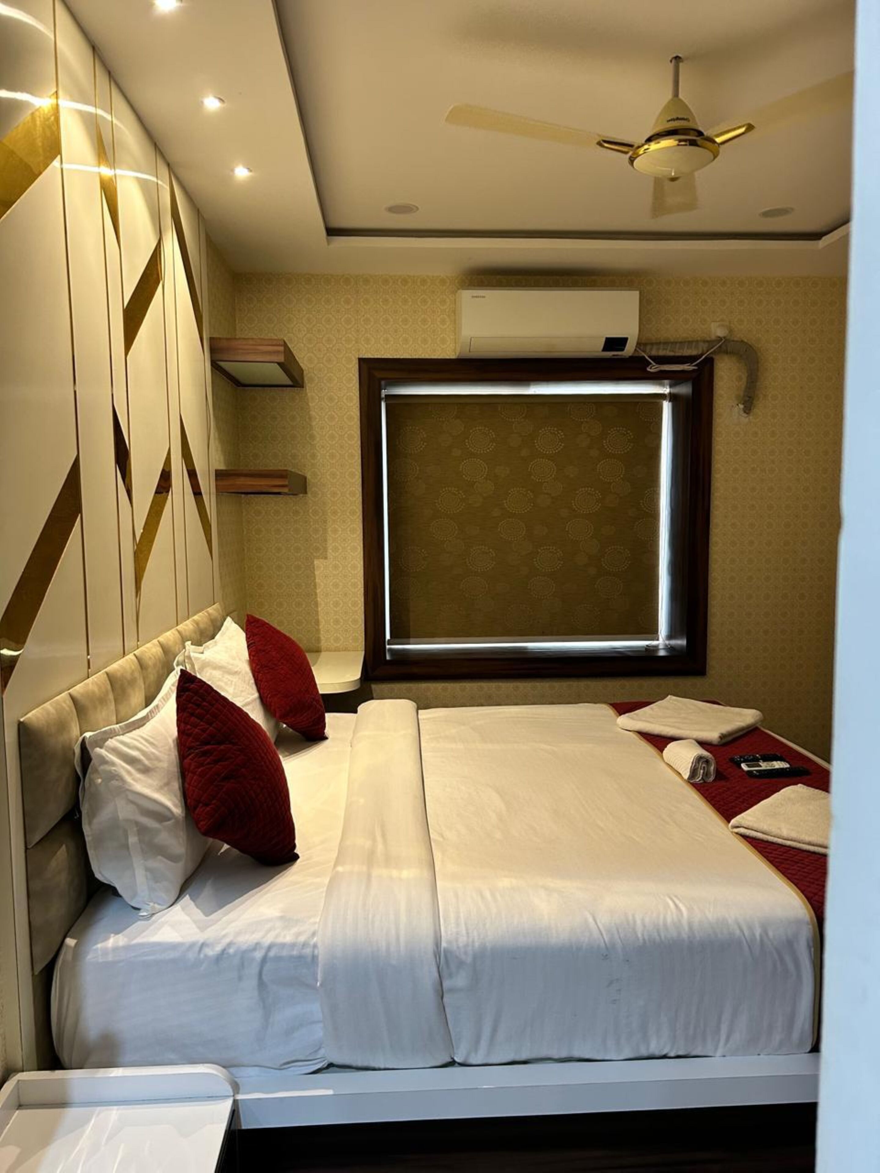 A hotel room with a bed, pillows, a ceiling fan, and a window.