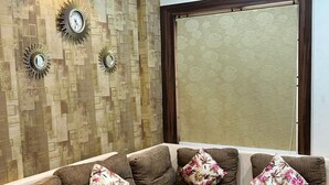 A modern living room with a sectional sofa, decorative wall clocks, and a large window. - Jagannath Puri Beach Stay (Brahmagiri)