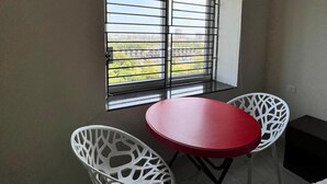 A small room with a red table and two white chairs, a window with blinds, and an air conditioning unit. - Jagannath Puri Beach Stay (Brahmagiri)