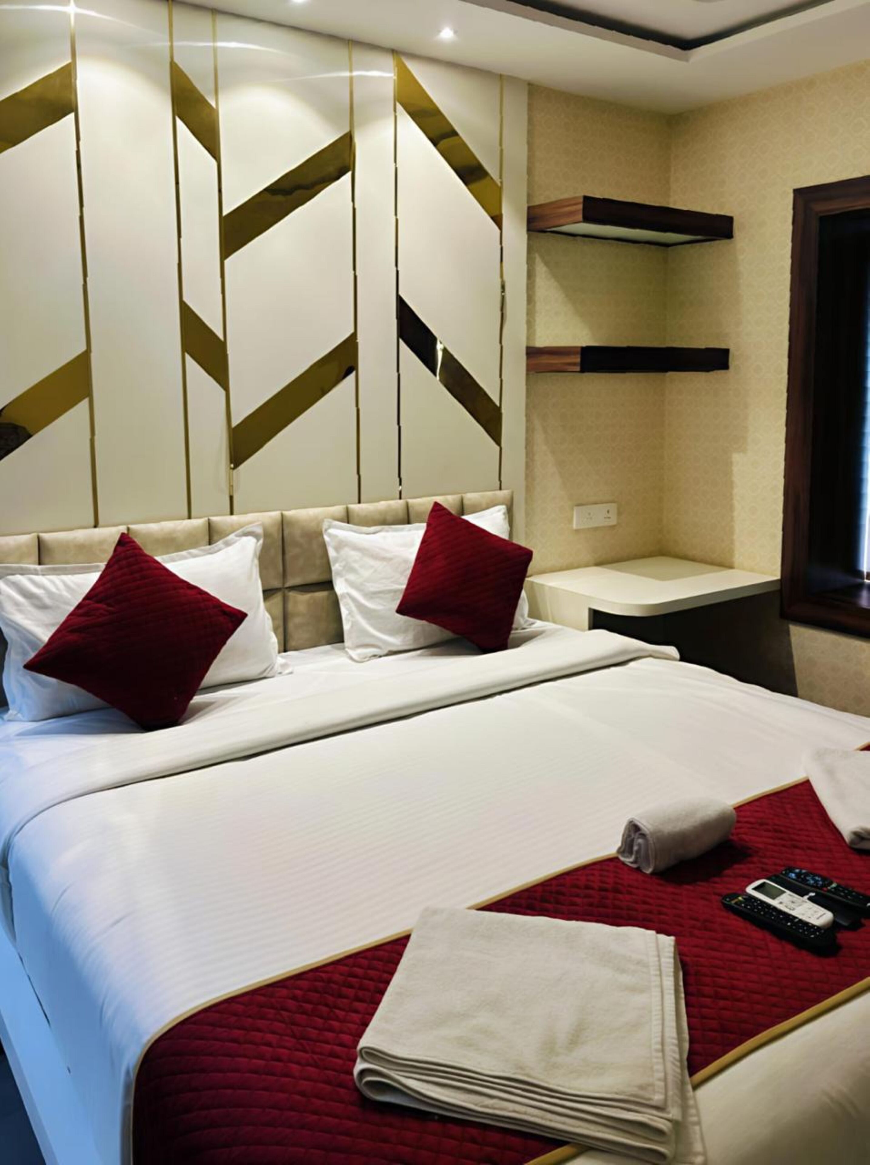 A hotel room with a bed, a red quilted bedspread, white linens, and a remote control on the bed.